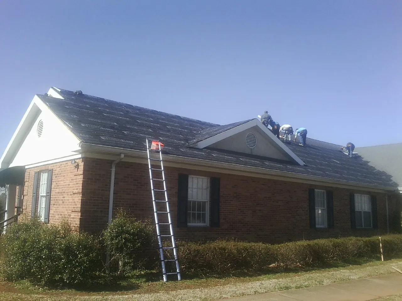Crew tearing shingles off a brick ranch roof with a ladder set — Emergency Roof Repair work by our crew in Baxter