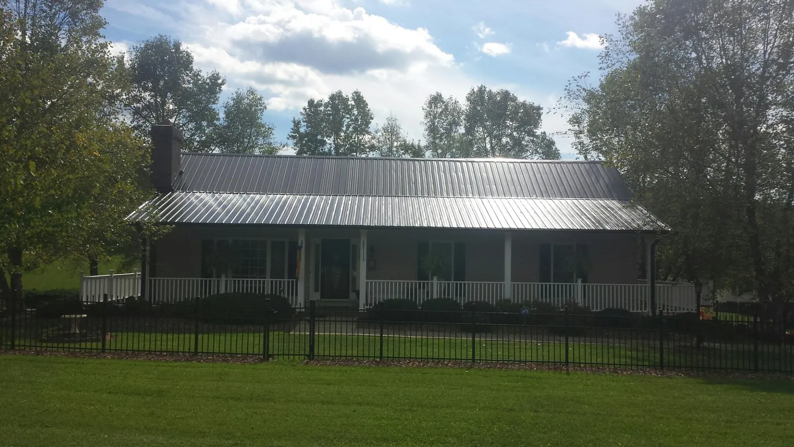 Gray metal roof on a brick ranch with a full width front porch — Gutter Guard Installation work by our crew in Baxter