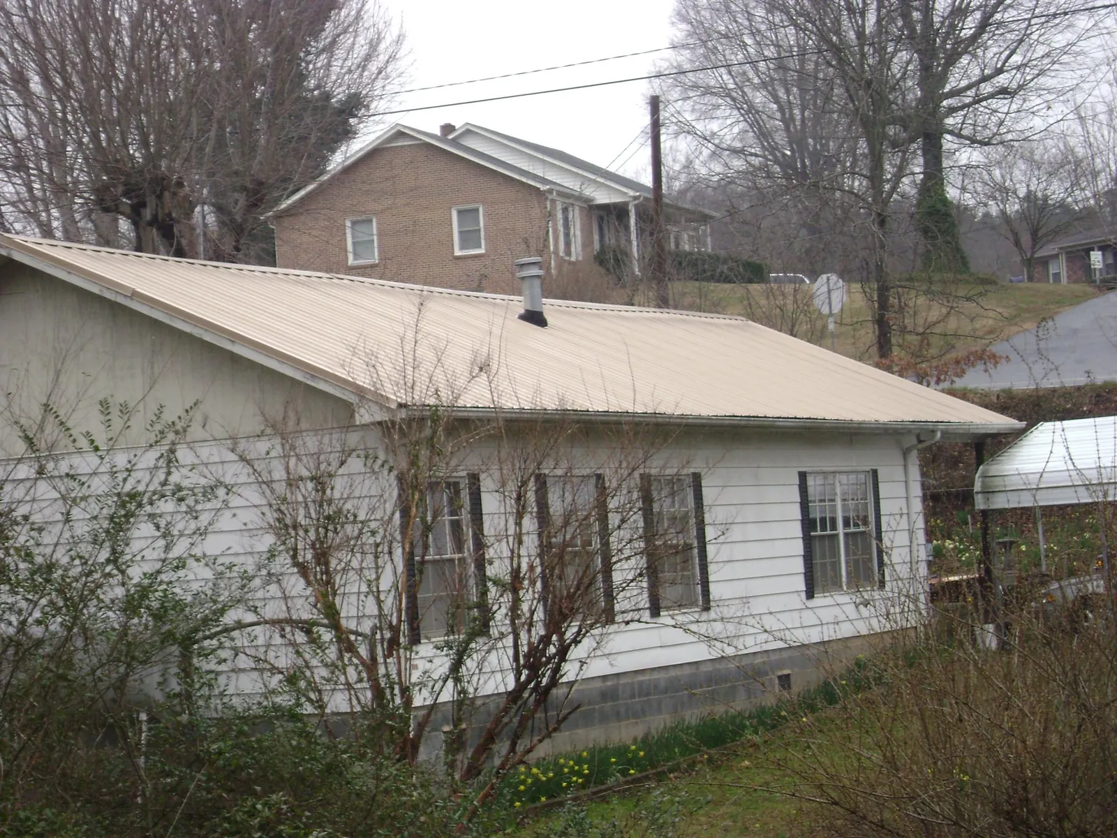 Tan metal roof on a white sided house set into a hillside — Commercial Roofing by Roofing Brothers in Baxter
